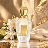 A luxury perfume bottle named 'Shooting Stars LUA' by the brand 'VIRGILIE', styled with white flowers, lime slices, and draped gold fabric on a marble surface.