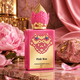 Pink Boa perfume bottle by Stephane Humbert Lucas, featuring a bright pink body, a gold honeycomb heart design with blue gem eyes, and a gold crown-shaped cap, styled on a marble surface with pink flowers and draped satin fabric.