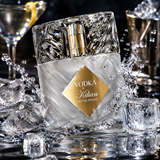 A clear glass bottle with a textured, faceted cap and a gold label reading 'VODKA by Kitian ON THE ROCKS,' surrounded by ice cubes and water splashes in a dark, reflective setting.