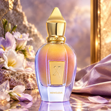 Newcleus perfume bottle with a gold cap and iridescent lavender-gold liquid, styled on a reflective surface with flowers and draped fabric in a warm, luxurious setting.