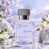 A clear glass perfume bottle labeled Maison Francis Kurkdjian Paris Aqua Celestia, with a silver cap, centered against a soft sky-blue background with white flowers and pale purple blossoms around it.