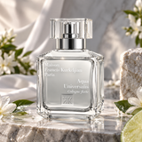 A clear glass perfume bottle with a silver pump and transparent cap, labeled Maison Francis Kurkdjian Paris Aqua Universalis Cologne forte, styled on a marble surface with white flowers and soft draped fabric in the background.