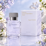 Maison Francis Kurkdjian Paris Aqua Celestia Eau de Toilette perfume bottle and its white packaging box, styled with white and purple flowers on a reflective surface.