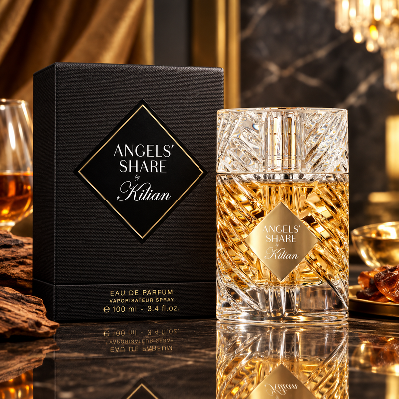 Angels' Share by Kilan Eau de Parfum shown with its black textured box and the clear faceted perfume bottle filled with golden liquid, set on a reflective surface in a warm luxury interior.