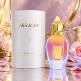 Xerjoff Newcleus Limited Edition perfume bottle and its white cylindrical packaging box, styled with pink roses and gold accents on a reflective surface.