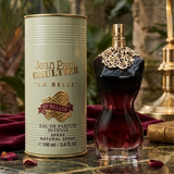 "A bottle of Jean Paul Gaultier La Belle Le Parfum Eau de Parfum Intense with its matching gold packaging box, set against an elegant background with greenery and warm natural lighting."