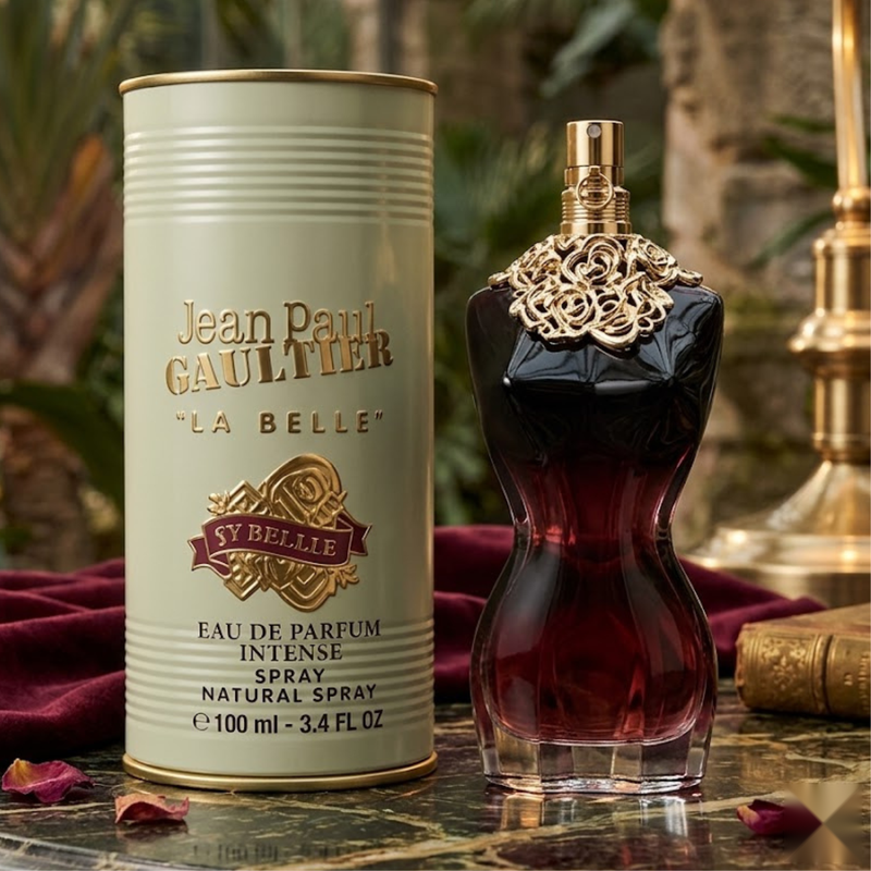 "A bottle of Jean Paul Gaultier La Belle Le Parfum Eau de Parfum Intense with its matching gold packaging box, set against an elegant background with greenery and warm natural lighting."