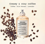 "A Maison Margiela Replica Coffee Break perfume bottle styled with coffee, red apple, lemon, lavender, peppermint, and other fragrance ingredients against a warm, elegant background."