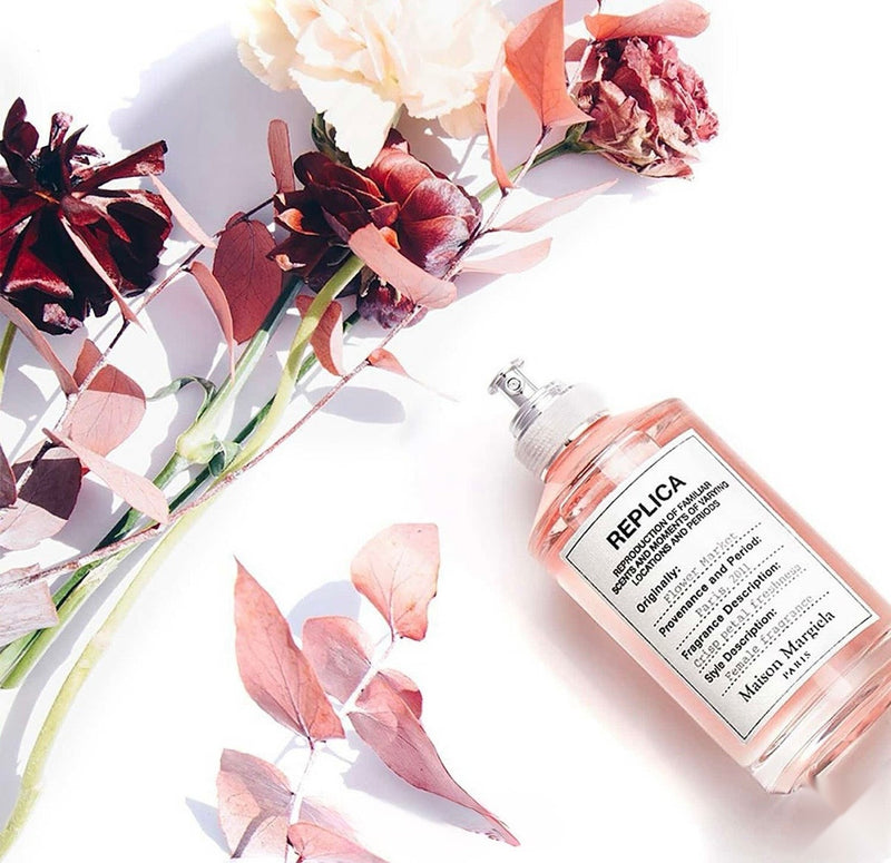 "A Maison Margiela Replica Flower Market perfume bottle with a cream-colored label, set against a soft floral background with natural lighting."