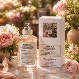 "A bottle of Maison Margiela Replica Flower Market Eau de Toilette with its matching packaging box, set against a lush floral background with soft natural lighting."