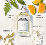 A perfume bottle labeled 'Replica From The Garden' by Maison Margiela, styled with green mandarin, grapefruit, blackcurrant, tomato leaf, geranium bourbon, rose, Indonesian patchouli, crystal moss, and white musk against a bright garden background with green leaves, citrus fruits, and soft natural lighting."