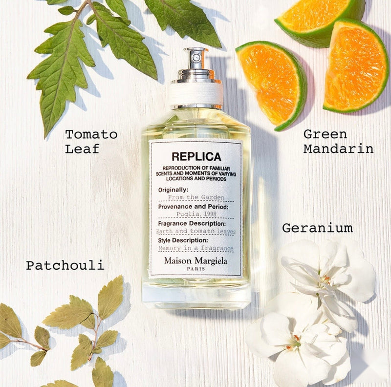 A perfume bottle labeled 'Replica From The Garden' by Maison Margiela, styled with green mandarin, grapefruit, blackcurrant, tomato leaf, geranium bourbon, rose, Indonesian patchouli, crystal moss, and white musk against a bright garden background with green leaves, citrus fruits, and soft natural lighting."