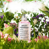 "A clear perfume bottle labeled 'Replica Springtime in a Park' by Maison Margiela, featuring a white label and silver cap, set against a bright spring garden background with green foliage, white flowers, and soft natural lighting."