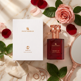 "A bottle of Swiss Arabian Rose 01 Extrait de Parfum with its matching white packaging box, featuring pink roses and other decorative flowers, set against a soft floral background with warm lighting."