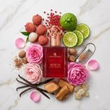 "A perfume bottle labeled 'Rose 01' by Swiss Arabian, styled with citrus slices, lychee, pink roses, spices, and other fragrance ingredients against a white marble background with soft lighting."