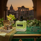 "A green perfume bottle labeled 'Born in Roma Donna Green Stravaganza' by Valentino, displayed against a dramatic architectural background with green foliage and warm golden lighting."