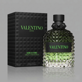 "A perfume bottle labeled 'Born in Roma Uomo Green Stravaganza' by Valentino, styled with Calabrian bergamot, coffee, vetiver, and other fragrance ingredients against a dramatic dark background with coffee beans, green citrus fruits, and warm lighting."